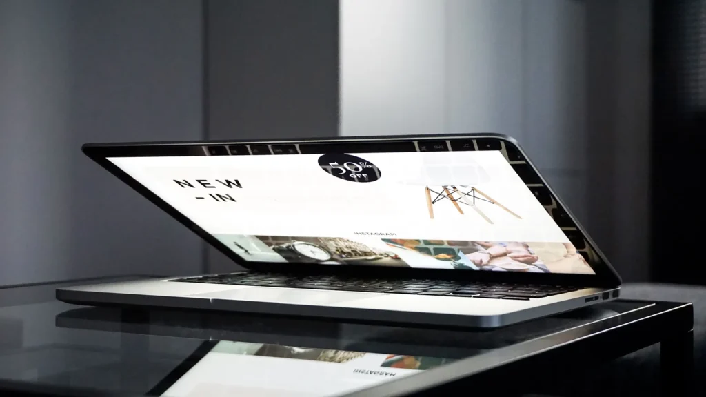 Laptop on a glass table displaying a website homepage