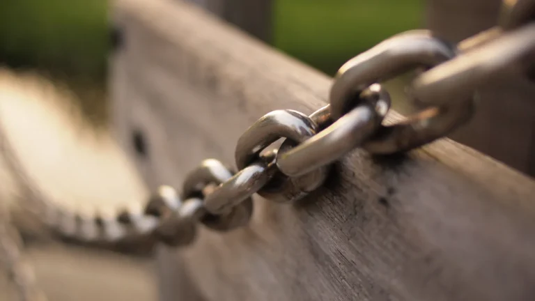 Close-up of connected metal chain links resting on a wooden rail, representing backlinks