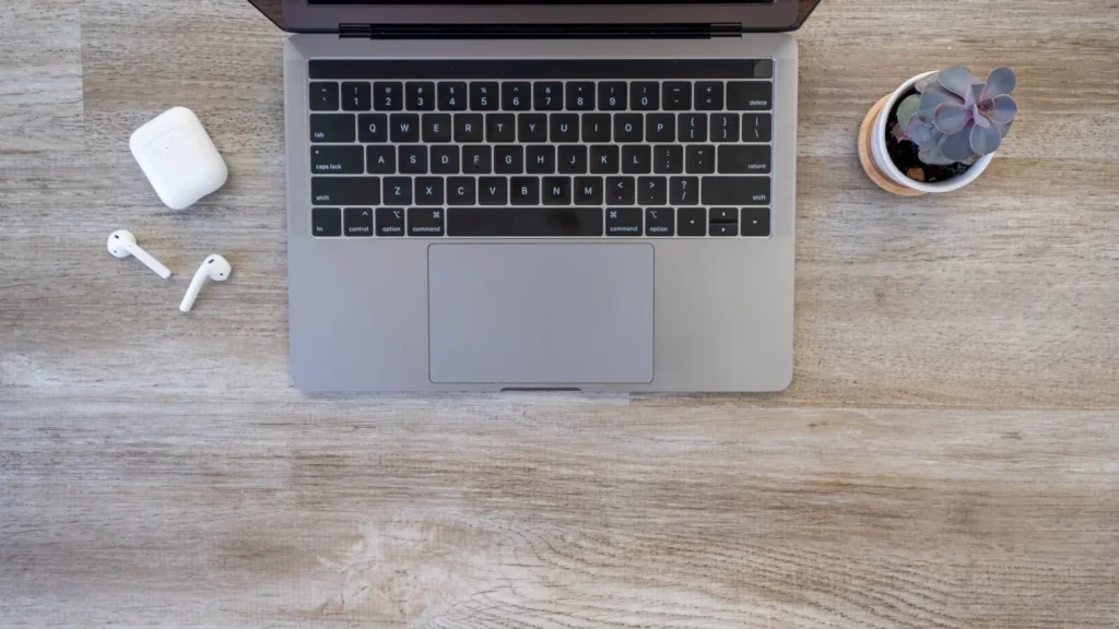 Top-down view of a tidy wooden desk with a laptop, wireless earbuds and a small succulent