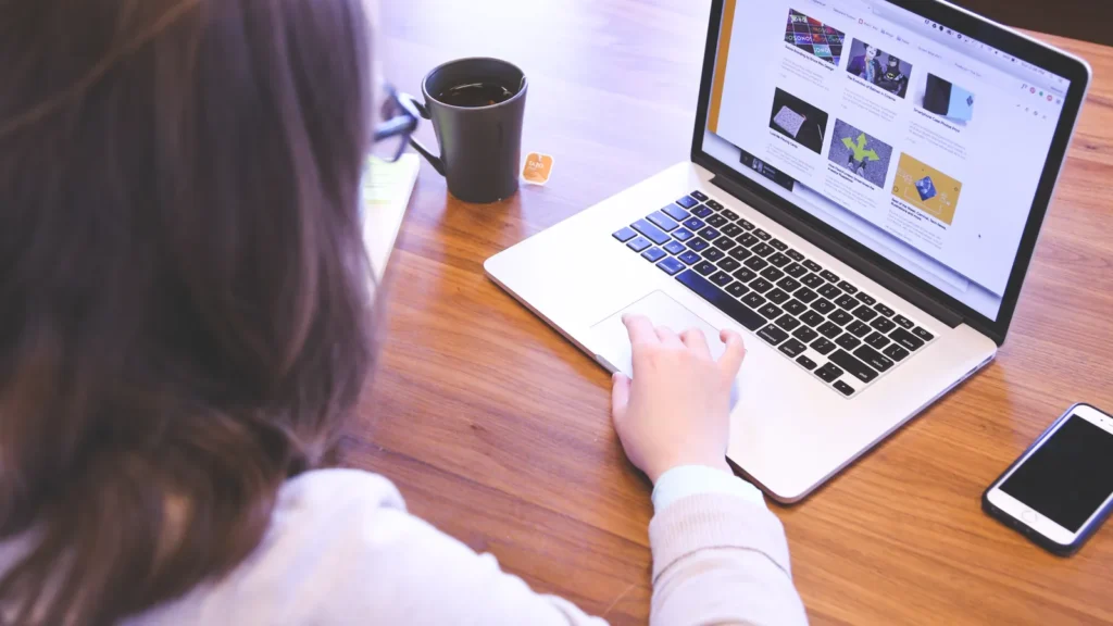 Person browsing websites on a laptop at a wooden table, representing an editor reviewing guest post pitches