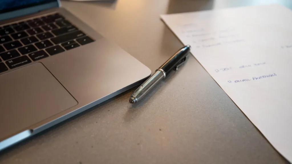 Laptop on a desk next to a pen and handwritten notes, used for drafting a guest post