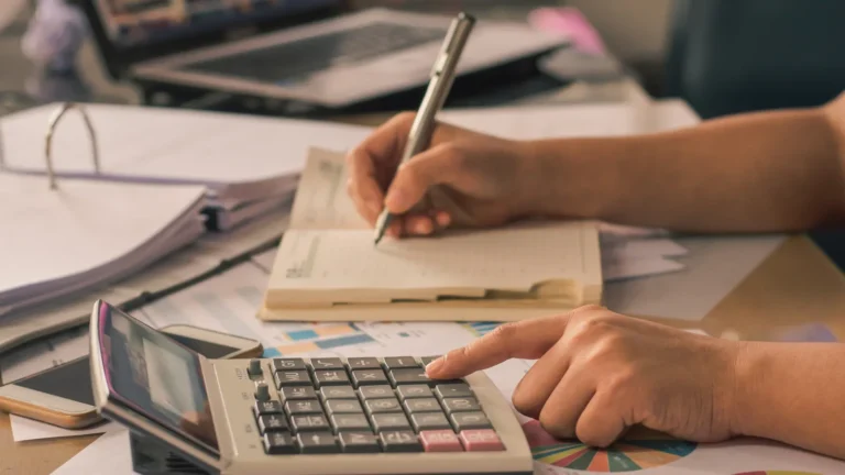 Person checking figures with a calculator and notebook over printed reports, representing vetting a website before guest posting