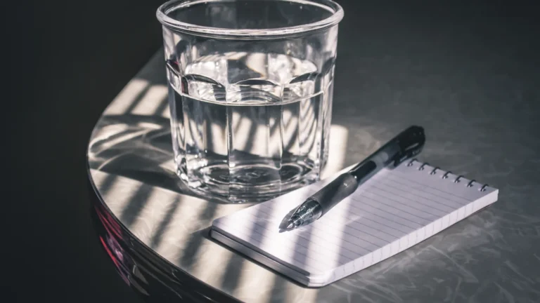 Blank notepad and pen beside a glass of water in sunlight, waiting for ideas