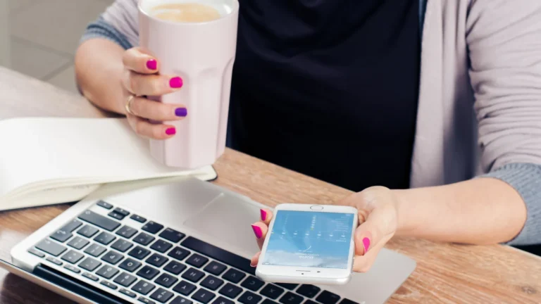 Person holding a smartphone and coffee beside a laptop and notebook, representing repurposing a blog post for several channels